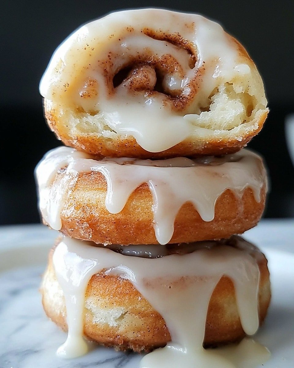 A stack of three cinnamon rolls is shown on a white marbled surface. The bottom roll is covered with thick, pale white icing that drips slowly down the side. The middle roll has the same icing spreading over its top and spilling slightly down its sides, revealing a soft, golden brown dough with cinnamon flecks. The top roll is smaller and partially eaten, showing its fluffy inside with a swirl of cinnamon filling. The icing on this top roll is also glossy and dripping lightly. The background is dark, making the cinnamon rolls stand out clearly, photo taken with an iphone --ar 4:5 --v 6.1