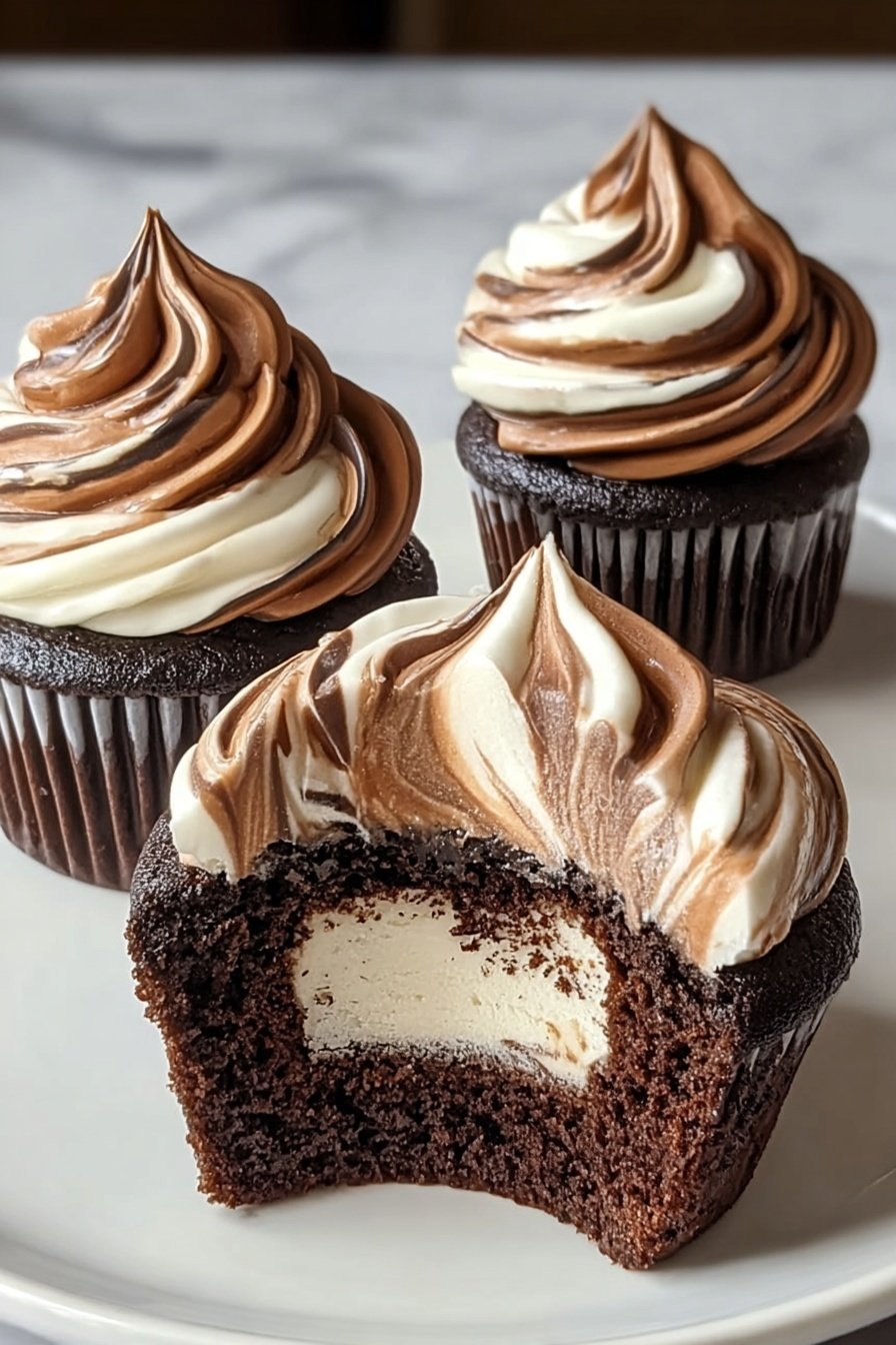 Chocolate Coffee Cream Cupcakes with Ganache Topping, chocolate coffee cupcakes, coffee filled cupcakes, ganache topped cupcakes, chocolate coffee dessert - The image shows three chocolate cupcakes on a white plate with a white marbled surface. Each cupcake has a dark chocolate base and is topped with two-tone swirled frosting in white and dark brown, with the swirls creating a soft, smooth texture. One cupcake is cut in half, showing the dark chocolate cake with a thick layer of creamy frosting that has inside the same white and brown swirl pattern. The other two cupcakes are whole, standing behind the halved cupcake. The lighting highlights the glossy texture of the frosting and the crumbly cake underneath. Photo taken with an iphone --ar 2:3 --v 7