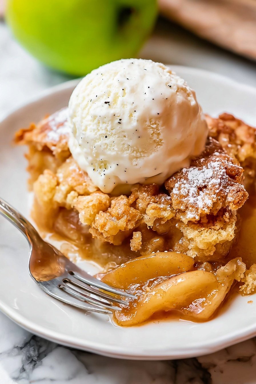Easy Apple Cobbler with Crispy Topping and Vanilla Ice Cream, apple cobbler dessert, quick apple cobbler recipe, homemade apple cobbler, apple desserts easy - The image shows a white plate holding a warm apple cobbler with golden brown, crispy, and bumpy topping that looks soft inside, decorated with light dusting of powdered sugar. Beneath the crunchy top, there are thick, soft, glossy apple slices in caramel color with cinnamon specks. On top of the cobbler is a big scoop of creamy white vanilla ice cream with small black vanilla bean dots, looking cold and smooth. A shiny silver fork lies on the left side of the plate. The plate rests on a white marbled surface, with a blurred green apple visible in the background. Photo taken with an iphone --ar 2:3 --v 7